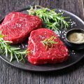 uncooked beef steaks with rosemary and finely ground black peppercorn on a black stone plate, landscape view from above