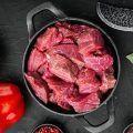 Irish raw Beef Stew Recipe ingredients set with sweet bell pepper, in cast iron frying pan, on black stone background, top view flat lay